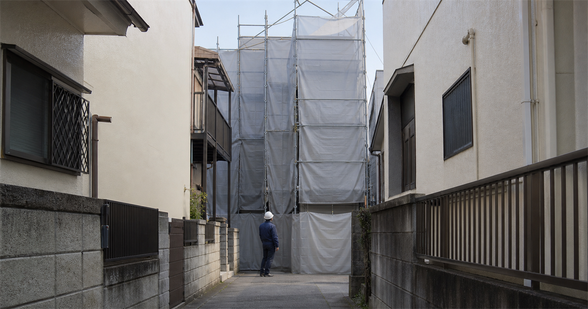 住宅が密集した細い路地の奥で足場に覆われた3階建て住宅の建替え現場。狭小地の工事が中心になる街