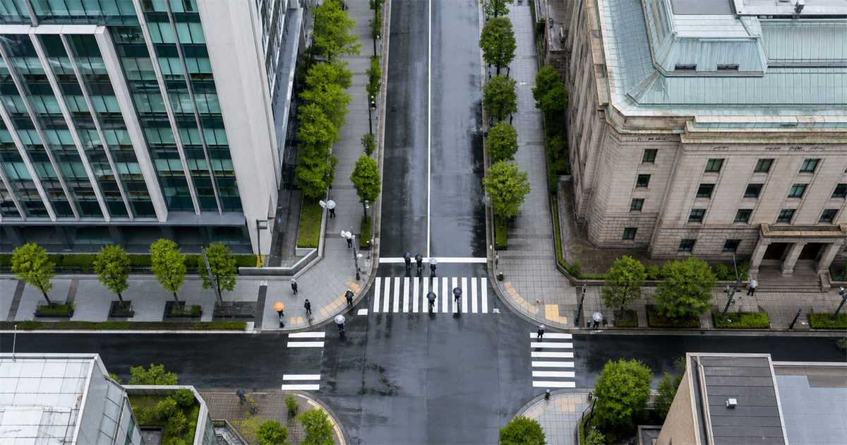 道路を挟んで向かい合う2棟の官公庁庁舎を俯瞰。許可行政庁と入札審査部門が別レイヤーであることを示すイメージ