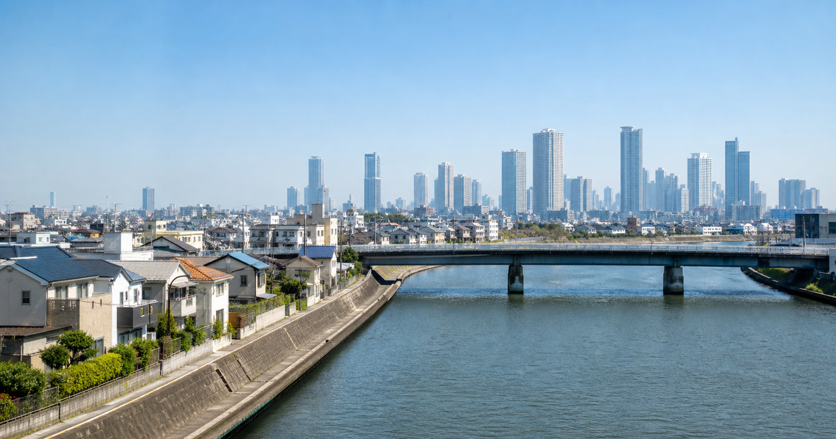 手前が低層住宅地、川と橋を挟んで奥に都心の高層ビル群が広がる風景。営業所の所在地で許可区分が決まることを表す図