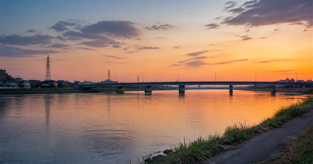 夕暮れの河川に架かる橋と両岸の街並み。八潮市が東京都足立区・葛飾区に接する都県境の立地のイメージ